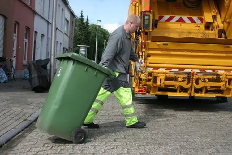 vuilnisman die een groene vuilcontainer naar de vuilniswagen brengt.